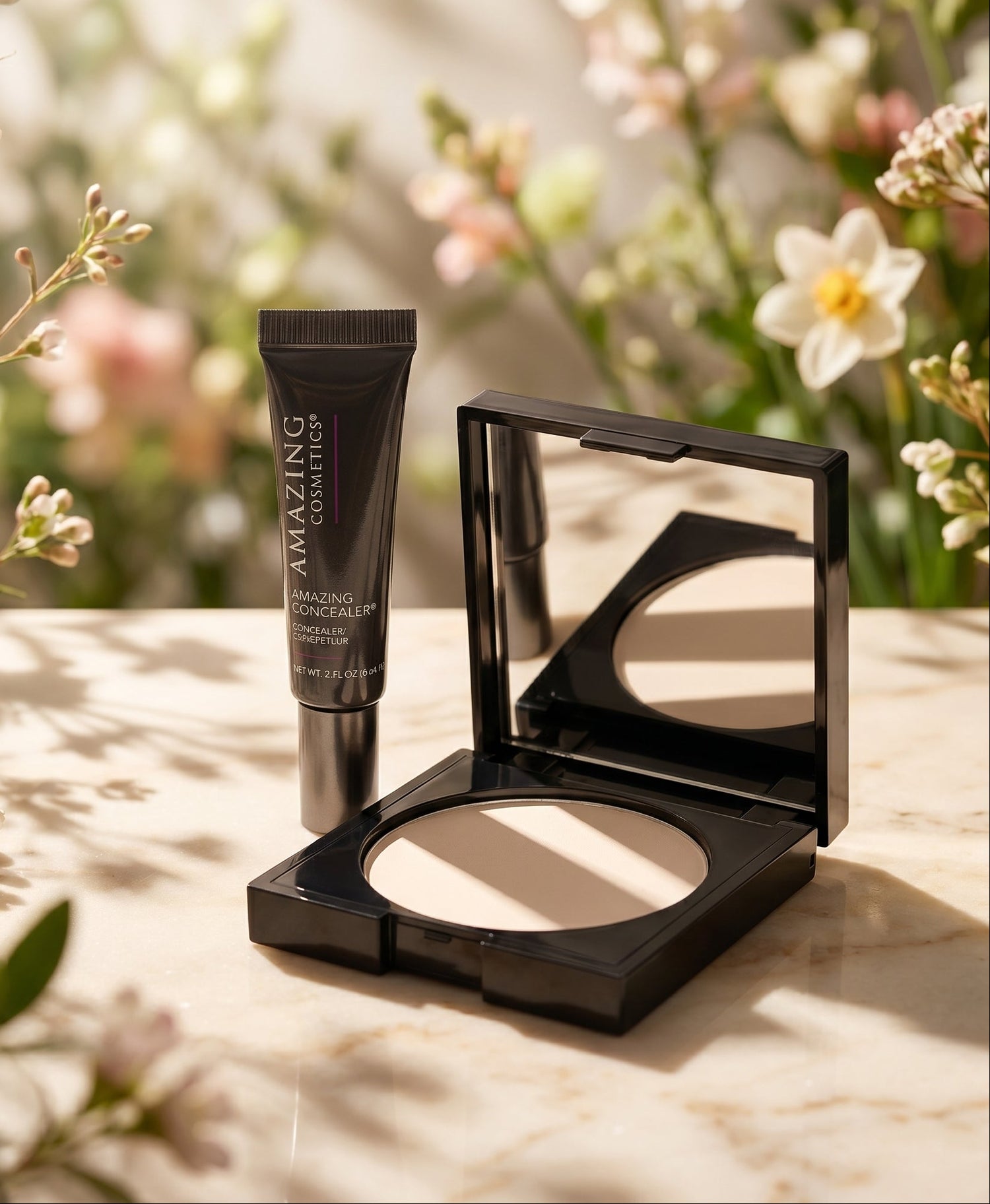 Makeup products including a compact powder and a tube on a surface with flowers in the background