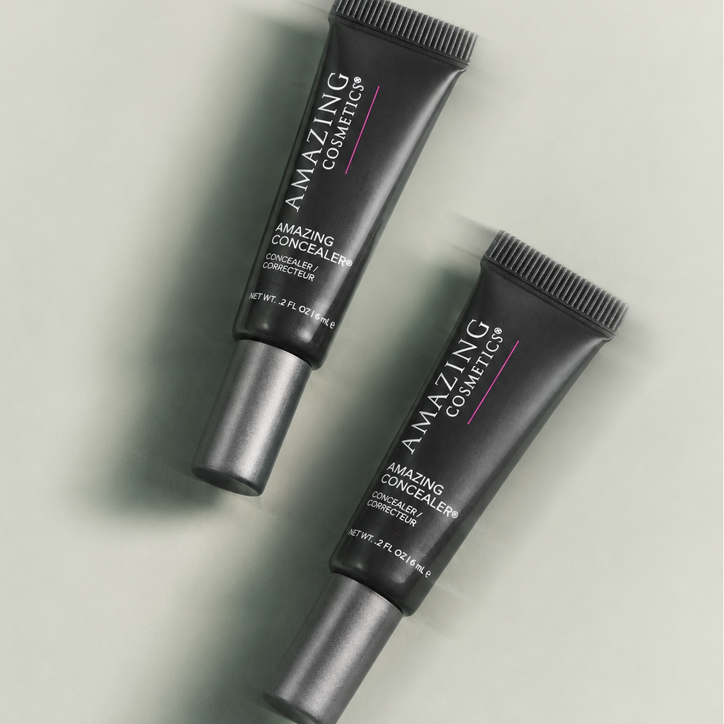 Two black squeeze tubes of Amazing Cosmetics Amazing Concealer with silver caps, arranged diagonally on a light gray background.